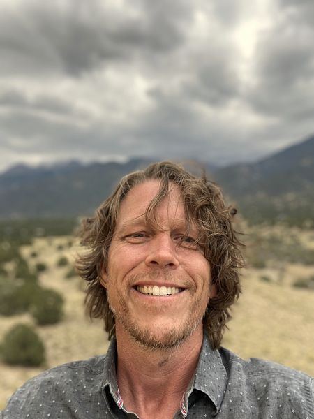 Sean smiling outdoors, mountains and a cloudy sky behind him